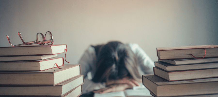 A student with their head in their hands behind two piles of books